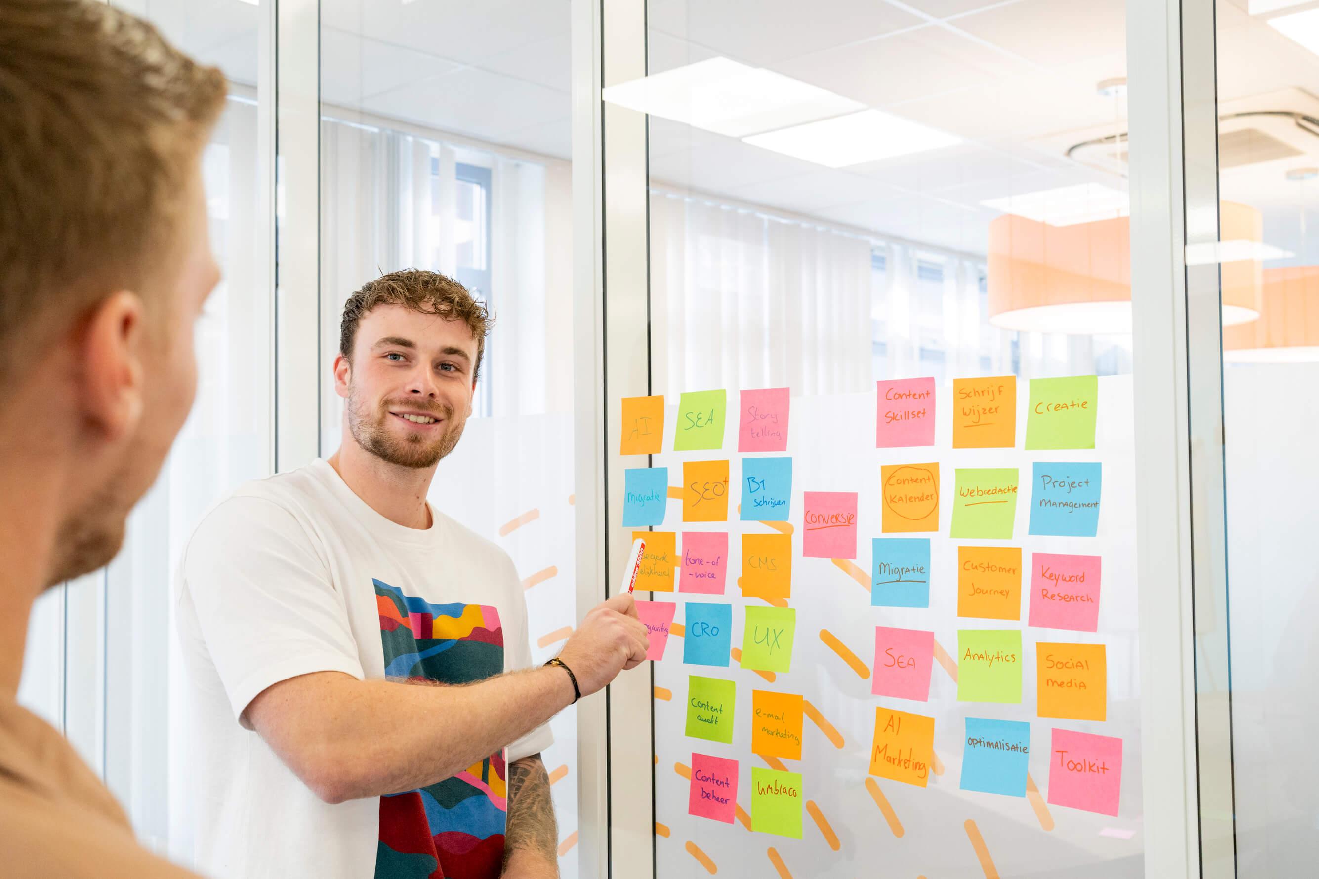 Man wijst naar een muur met post-its