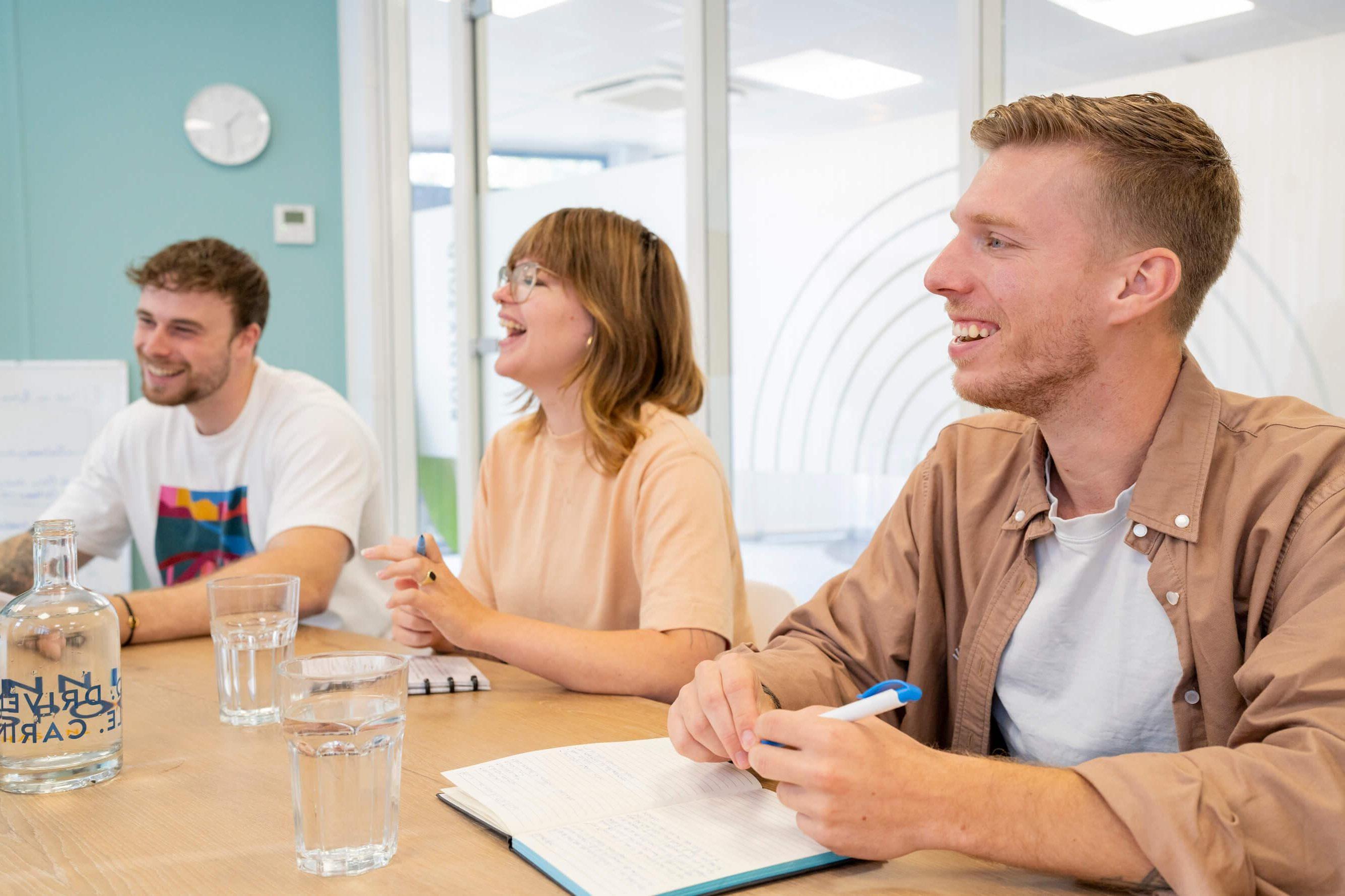 Drie collega's lachen tijdens een vergadering aan tafel