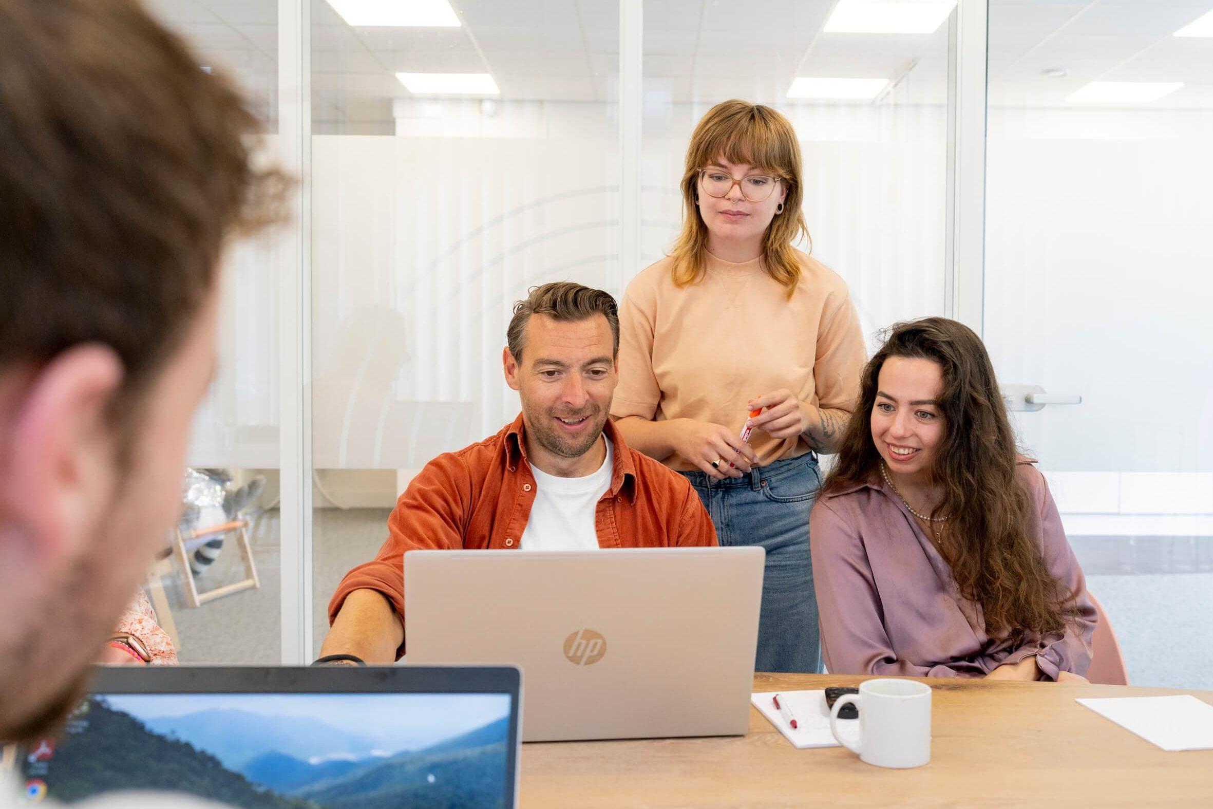 Collega's overleggen samen rond een laptop in een vergaderruimte