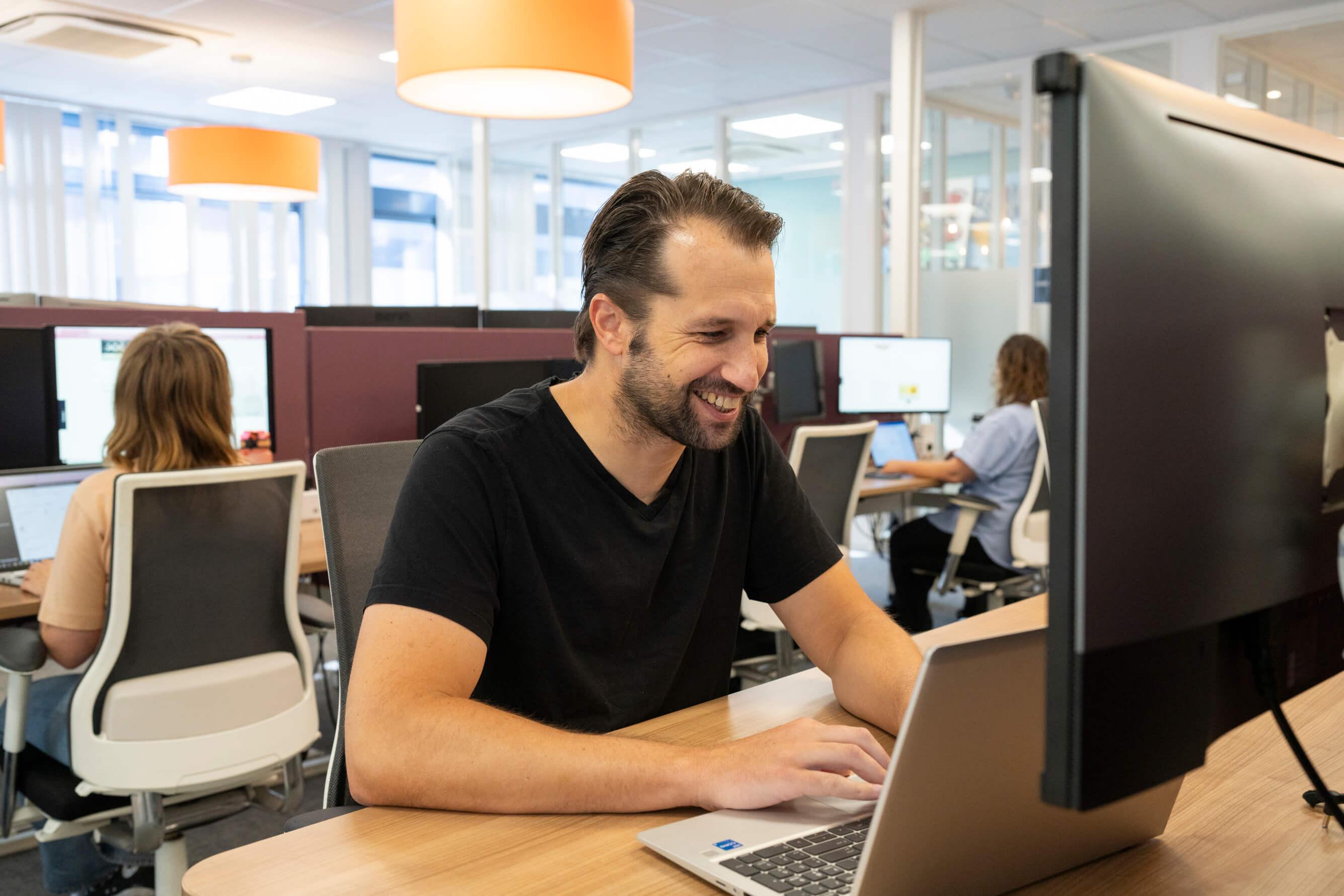 Man glimlacht terwijl hij op een laptop werkt