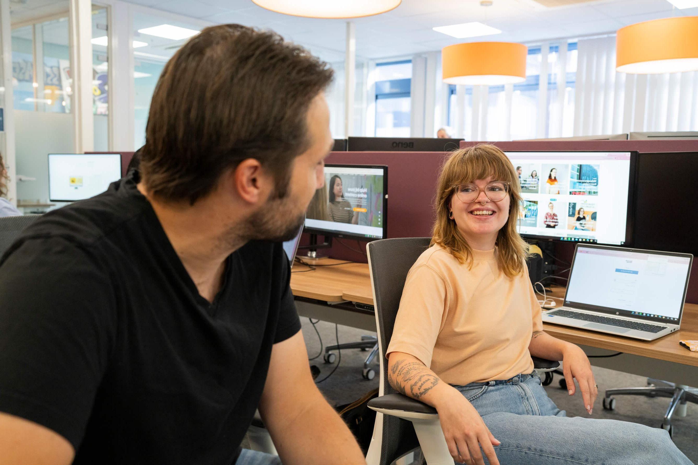 Persoon lacht naar collega aan een bureau