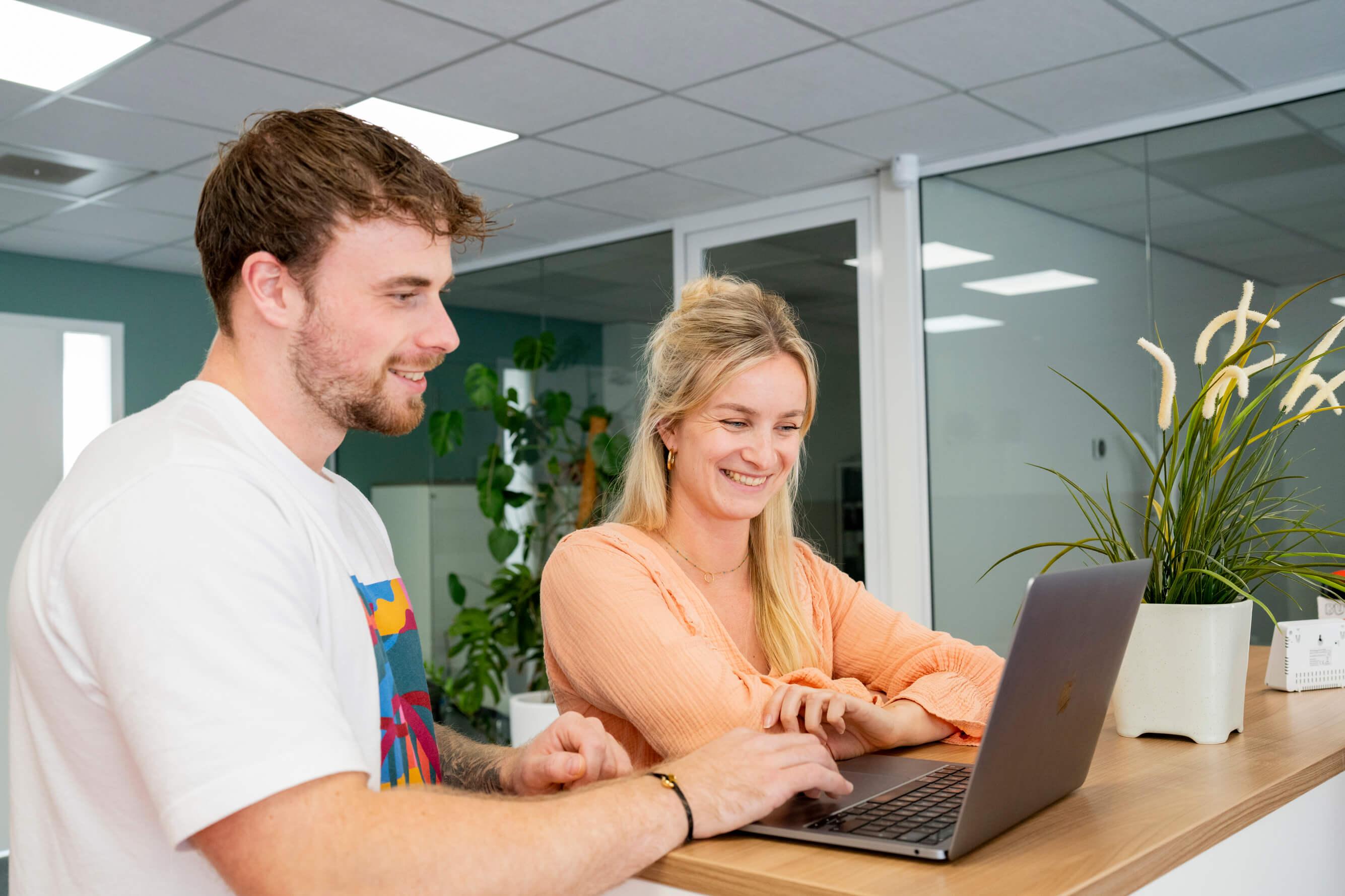 Twee lachende collega's werken samen achter een laptop