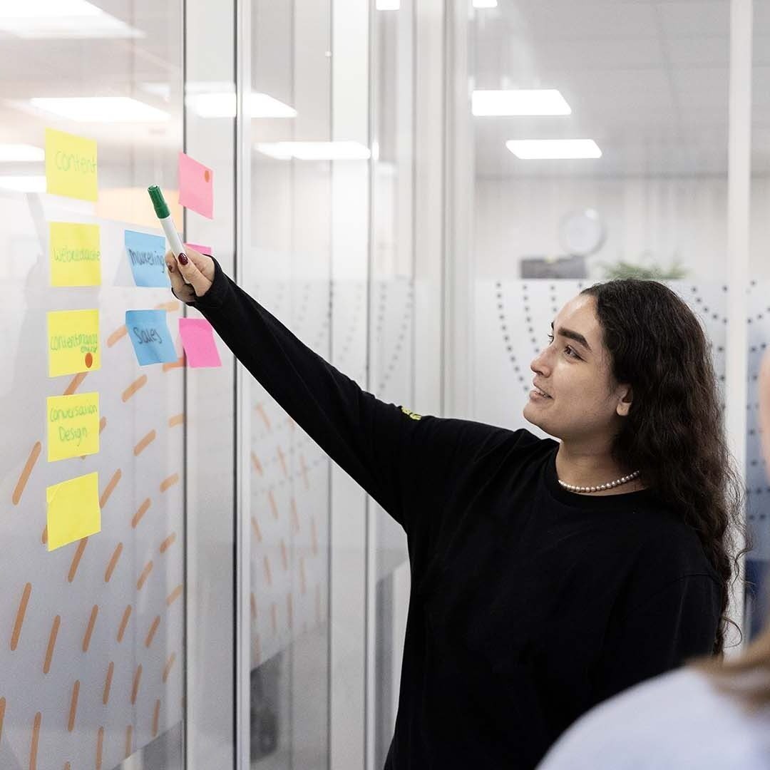 Collega wijst met een pen naar post-its op de muur